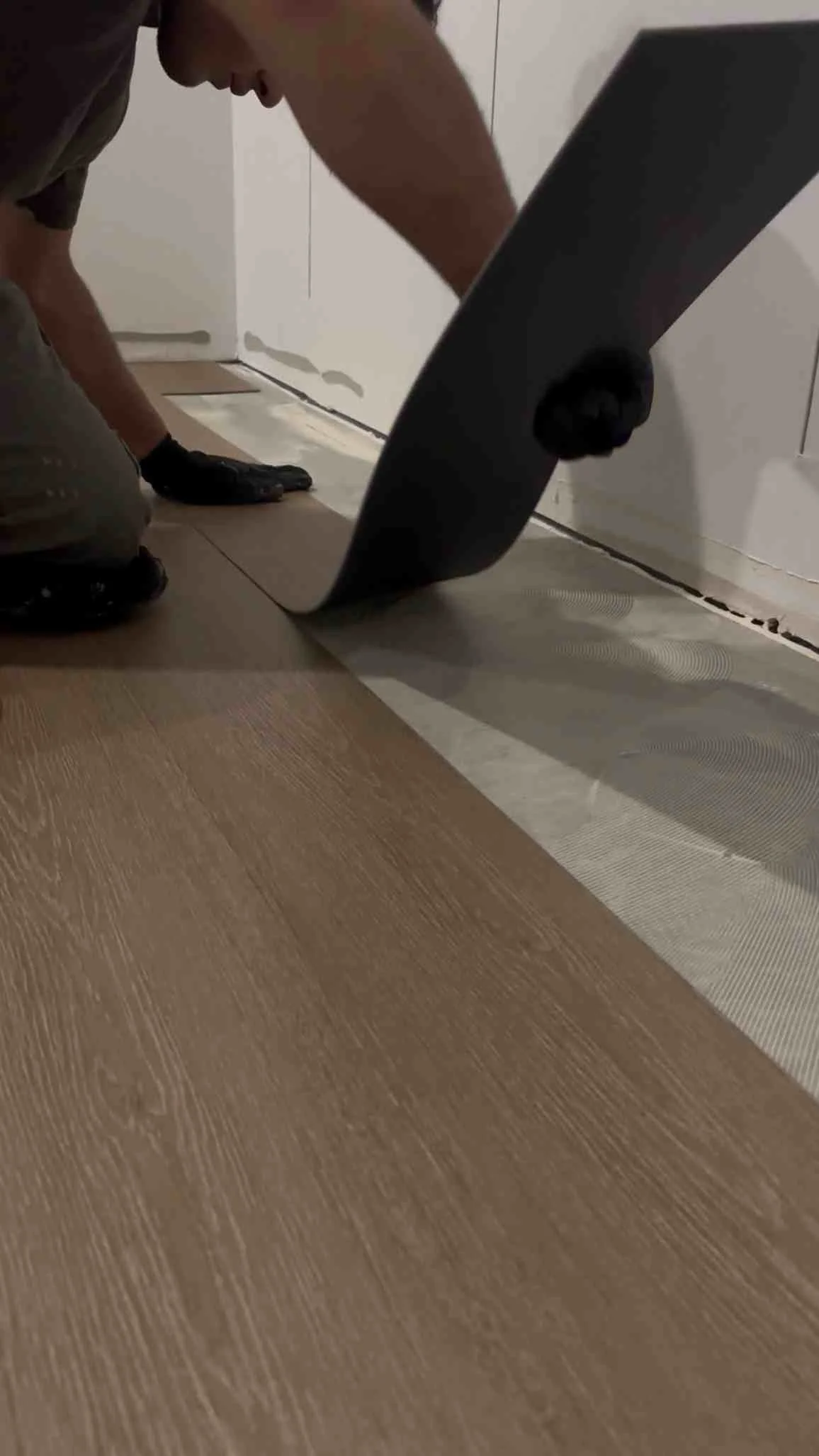 Worker installing luxury vinyl plank flooring with baseboard trim and transition strips