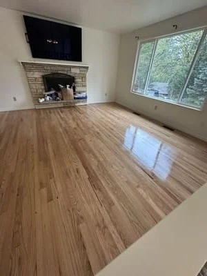 Newly installed hardwood flooring in living room with fireplace and large windows