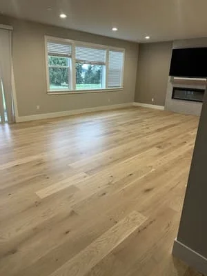 Light oak hardwood flooring in open living room with recessed lights and windows