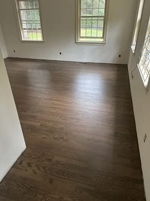 Dark hardwood flooring installed in room with white walls and windows