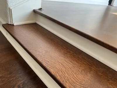 Medium-brown hardwood flooring with matching baseboard trim and white cabinetry edge detail