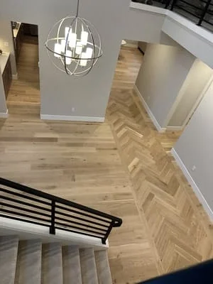 Herringbone pattern wood flooring in light oak with stair transition and modern pendant lighting