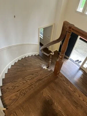 Oak hardwood flooring installed on curved staircase with wooden banister and metal handrail