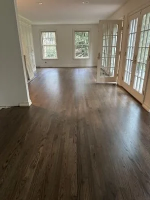Dark engineered hardwood flooring installed in open room with French doors and windows