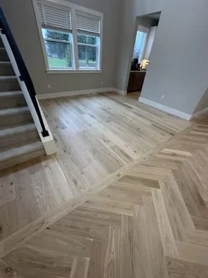 Herringbone pattern wood flooring in light oak tone with staircase and doorways visible