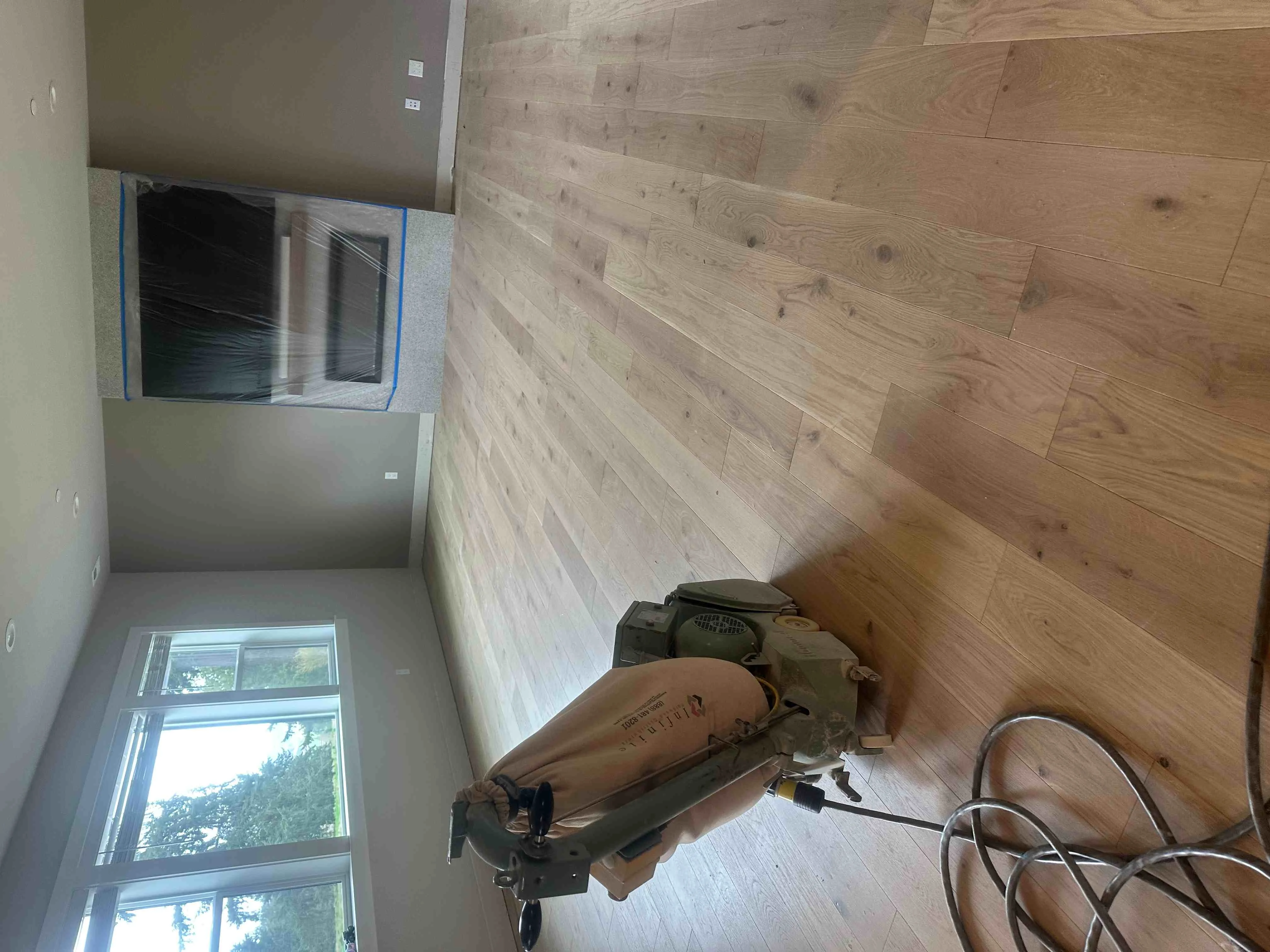 Light oak hardwood flooring installation with plank layout and pneumatic nailer on subfloor