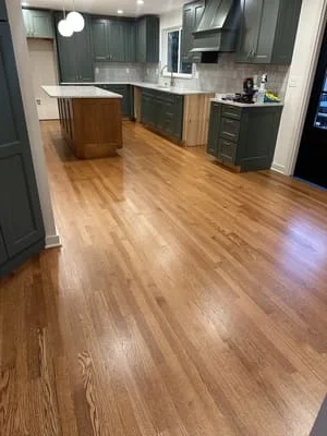 Newly installed warm oak hardwood flooring in kitchen with dark cabinetry and island